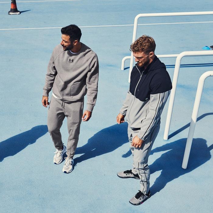 Two men in high end sportswear at a pale blue sports ground